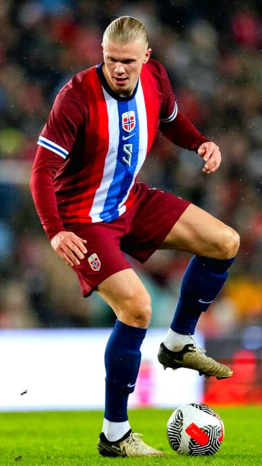 A male soccer player in a maroon and blue Norway national team jersey controls a soccer ball on the field during a match, as seen on Malta IPTV. The background is blurred.