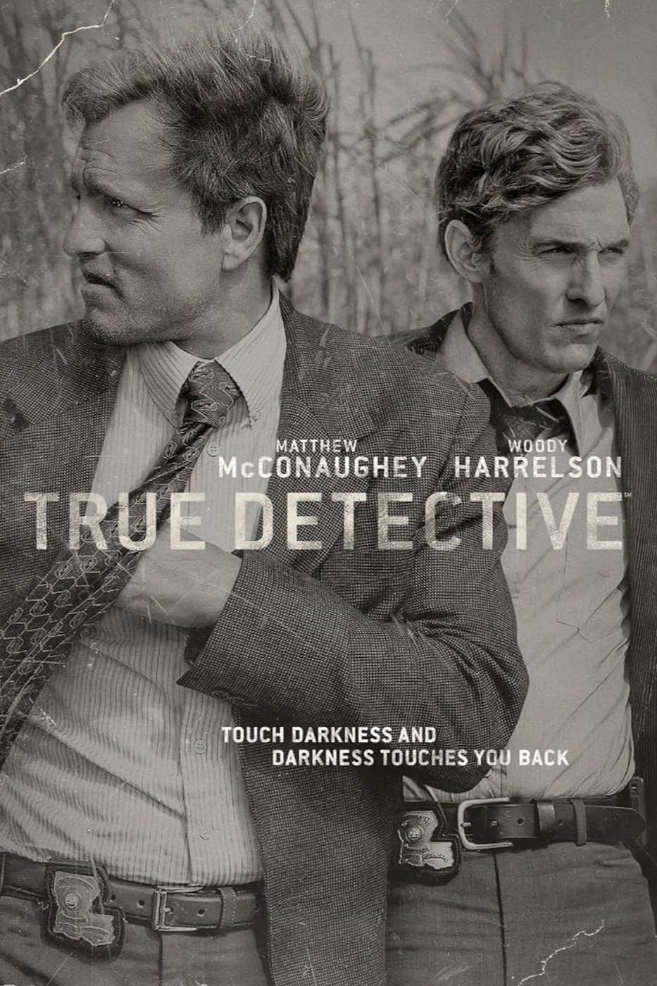 Two men in suits stand outside in tall grass, looking in different directions with serious expressions. The black and white image features the text “True Detective,” actors’ names, and a subtle nod to Malta IPTV streaming options.