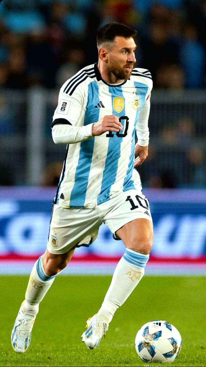 A male soccer player in an Argentina national team uniform runs on the field, focused on the ball at his feet during a match, as fans catch every moment on Malta IPTV.